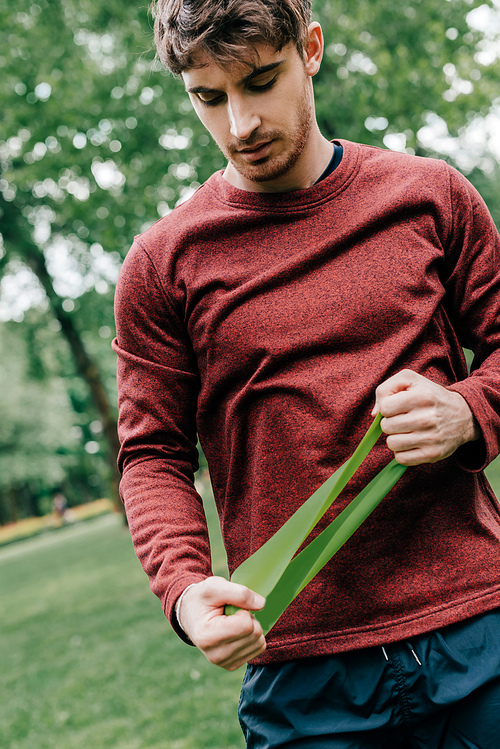 Handsome sportsman holding elastics band while working out in park