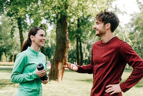 Smiling sportsman talking to girlfriend with sports bottle in park