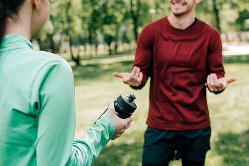 Cropped view of sportswoman holding sports bottle near smiling boyfriend in park