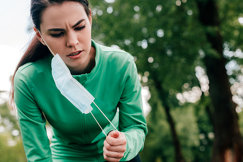 Young sportswoman taking off medical mask in park