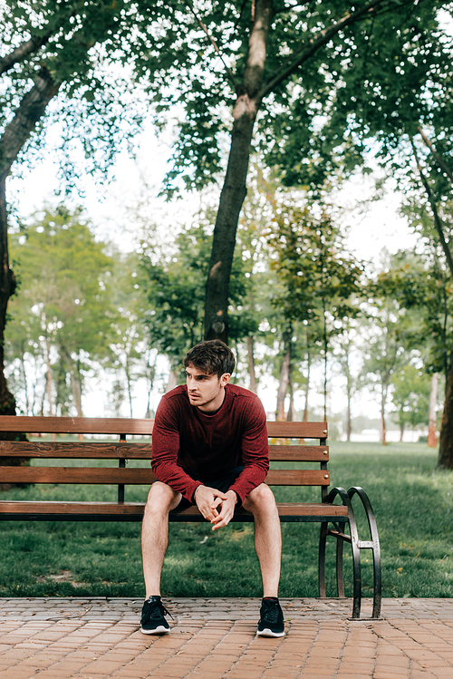 Handsome man in sportswear sitting on bench in park