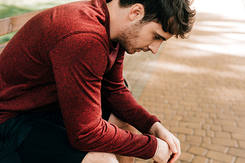 Side view of handsome sportsman resting on bench in park