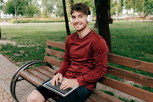 Smiling man in headphones  while using laptop in park