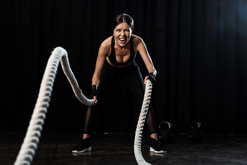 selective focus of sportswoman exercising with battle ropes on black