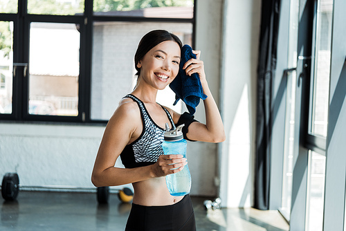 happy girl holding sport bottle while wiping sweat with blue towel