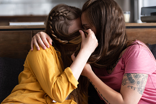 two lesbians covering faces with hair while embracing and kissing in living room