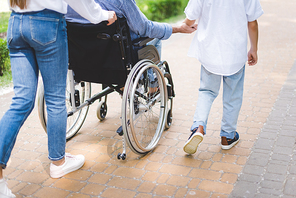 partial view of mother and son with disabled father on wheelchair in park