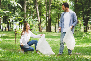 man and beautiful woman picking up garbage in plastic bags in park