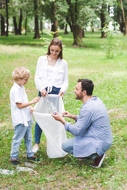 happy family picking up garbage in plastic bag in park