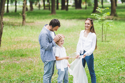 family in casual clothes picking up garbage in plastic bag in park