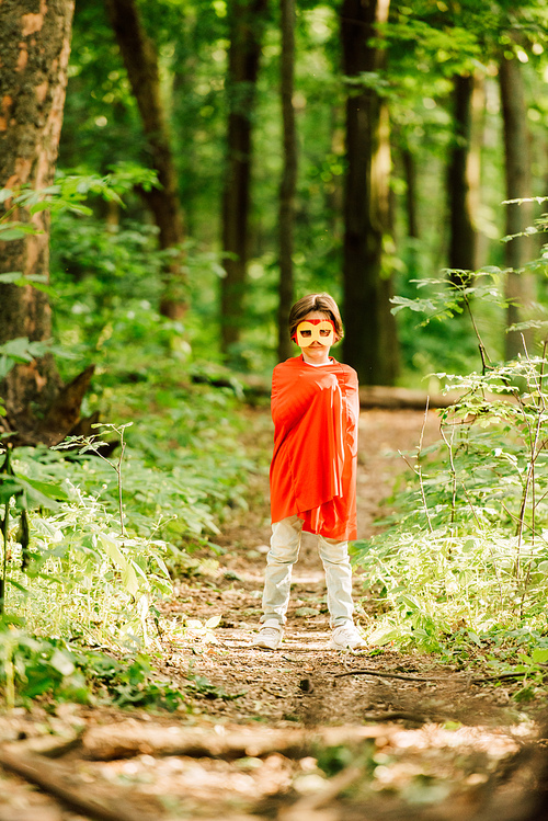 full length view of small boy in superhero costume standing in forest