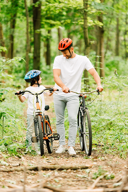 full length view of father and son walking with bicycles in forest