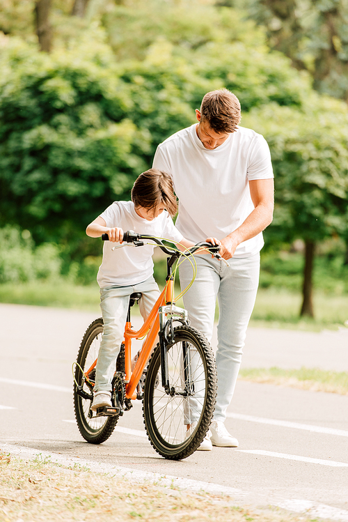 full length view of father looking at son while kid riding bicycle