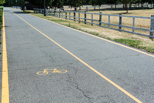 yellow symbol of bicycle lane on grey asphalt near fence