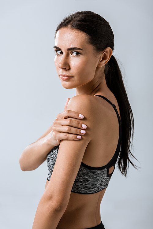 attractive brunette sportswoman with arm pain isolated on grey