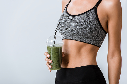 partial view of sportswoman holding smoothie isolated on grey