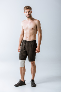 full length view of shirtless sportsman with elastic bandage on knee on grey