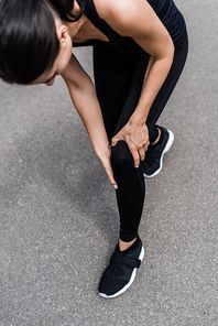 cropped view of sportswoman in black sneakers with knee pain on street