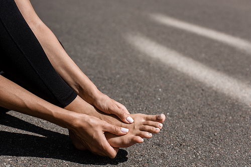partial view of barefoot sportswoman with foot pain on street