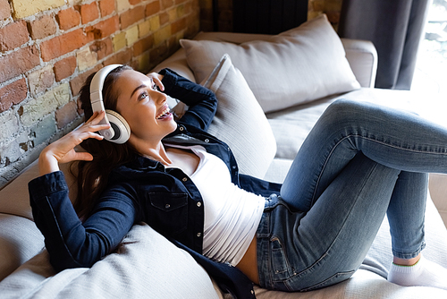 cheerful girl touching wireless headphones while listening music