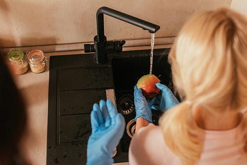 Selective focus of kid in latex gloves washing apple near mother