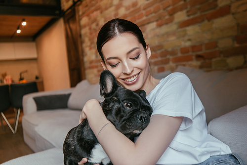 young woman with closed eyes hugging black french bulldog at home