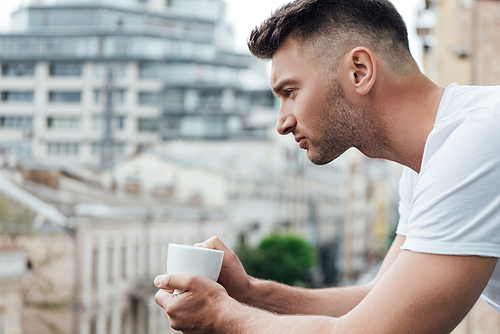 Side view of handsome man holding coffee cup on balcony