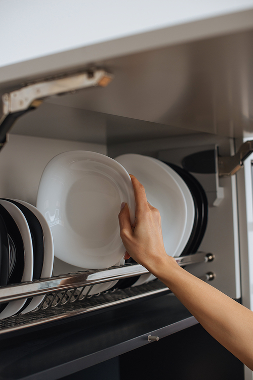 cropped view of housewife placing clean plate on rack in kitchen