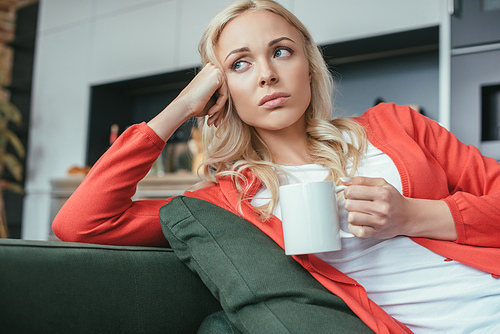 sad woman looking away while sitting on couch with cup of tea