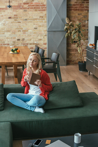 high angle view of pensive woman sitting on sofa, holding book and looking away