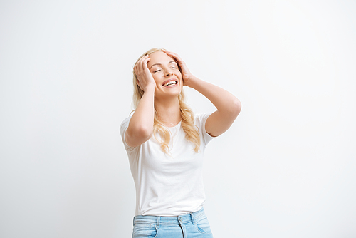 excited girl touching head while laughing with closed eyes isolated on white