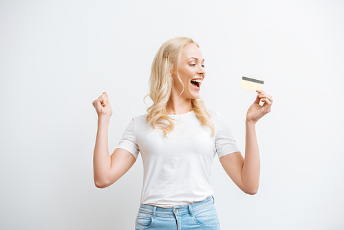 happy woman showing winner gesture while holding credit card isolated on white