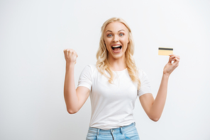 excited woman showing winner gesture while holding credit card isolated on white