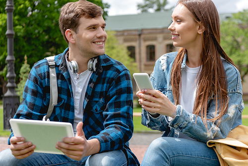 happy student and attractive girl holding gadgets and looking at each other