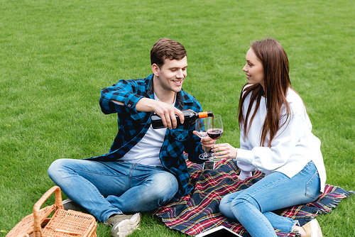 cheerful man pouring red wine near attractive girlfriend while having picnic