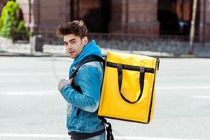 Side view of handsome courier with thermo backpack  on urban street