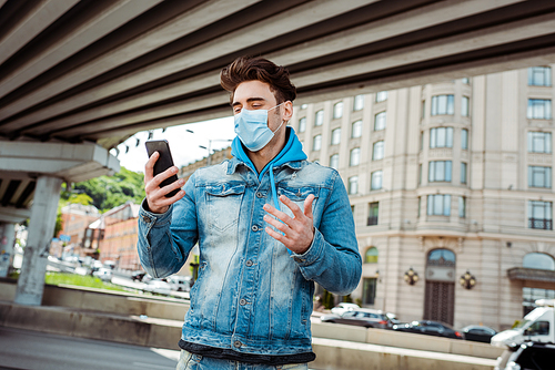 Man in medical mask holding cellphone on city street