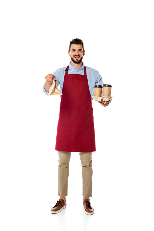 Handsome positive waiter holding paper bag and disposable cups on white background