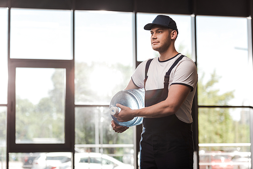 handsome delivery man in uniform and cap holding bottled water