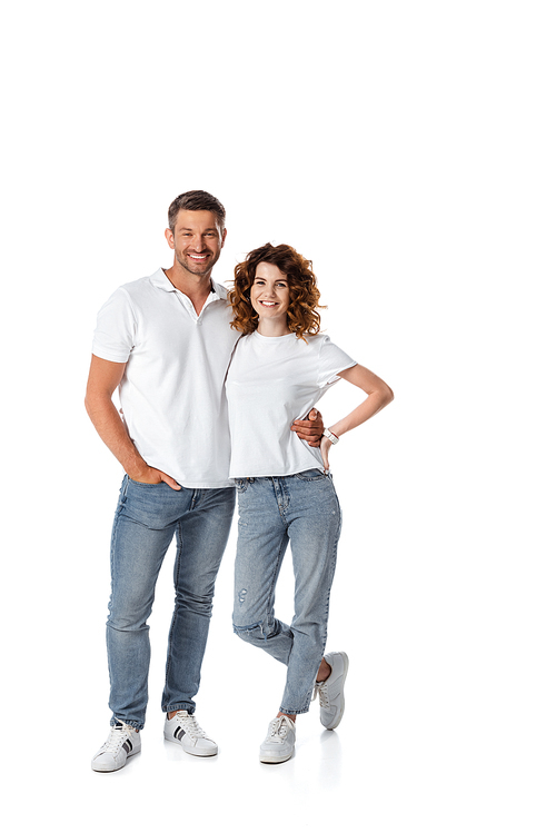 cheerful man standing with hand in pocket near wife with hand on hip on white