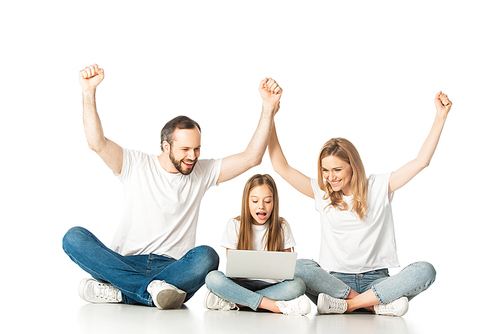 excited parents sitting on floor near happy daughter with laptop isolated on white