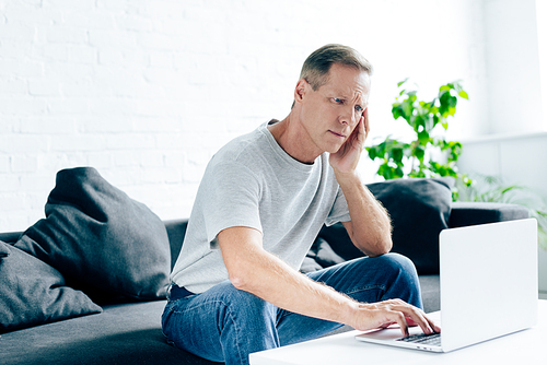 handsome man in t-shirt with headache using laptop in apartment