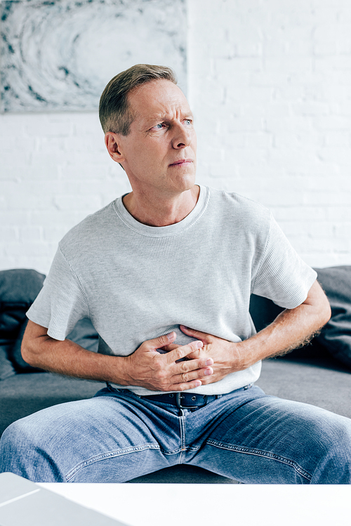 handsome man in t-shirt with stomachache looking away in apartment
