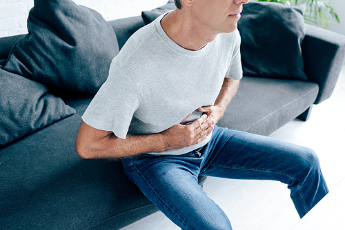 cropped view of man in t-shirt with stomachache in apartment