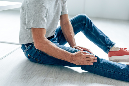 cropped view of man in t-shirt feeling pain in knee in apartment