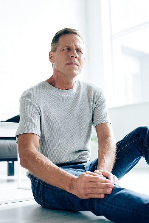 handsome man in t-shirt feeling pain in knee in apartment