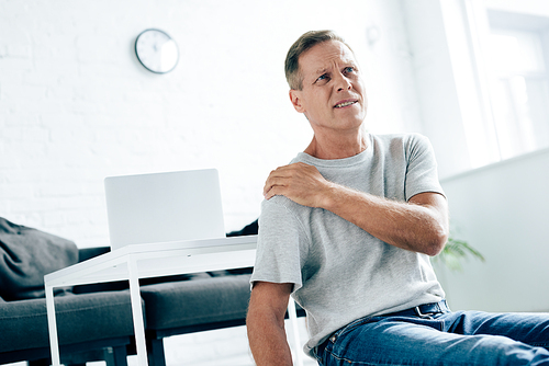 handsome man in t-shirt feeling pain in shoulder in apartment
