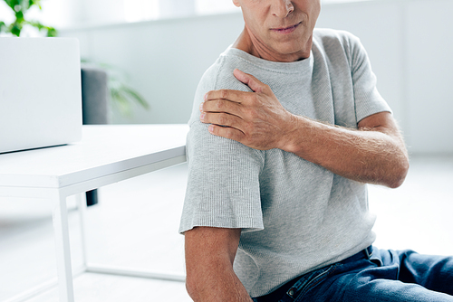 cropped view of man in t-shirt feeling pain in shoulder in apartment