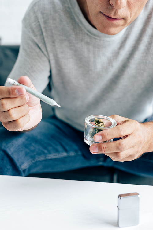 cropped view of man in t-shirt holding blunt and medical marijuana buds