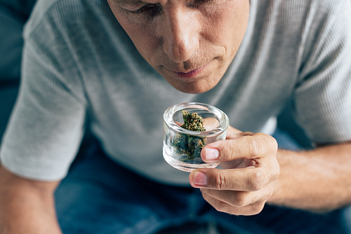 cropped view of man in t-shirt smelling medical cannabis in apartment